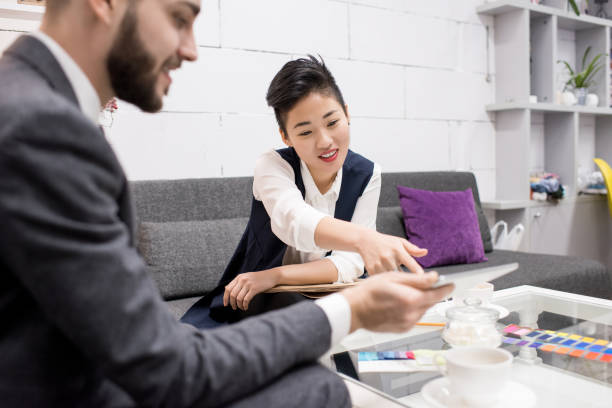 Two tailors discussing fabric swatches and measurements in a professional setting.